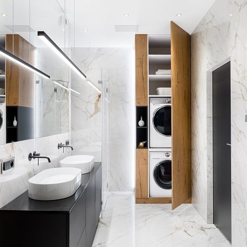 Elegant bathroom with marble floor and washing machine and clothes dryer in wooden closet